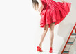young lady in red dress and red shoes with vintage tan stockings at red ladder on white background