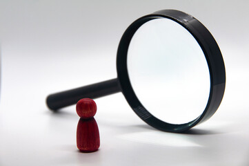 Red wooden figure looking through a magnifying glass with white background