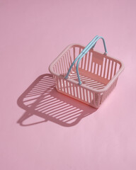 Plastic supermarket basket on pink background with shadow. Minimal shopping concept