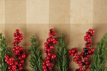 Canvas Print - Red berries and Christmas greenery on rustic tan plaid background for holiday banner with copy space.