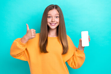 Photo of little teen girl wear stylish yellow sweatshirt hold smartphone empty space thumb up like shopping ad isolated on cyan color background