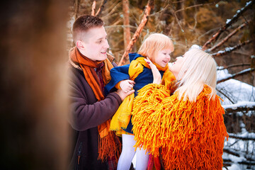 Wall Mural - Family including father, mother, little daughter in yellow, red and brown dress on a walk in winter. A man and woman couple and a young girl having play, fun, and walk outdoors in cold time