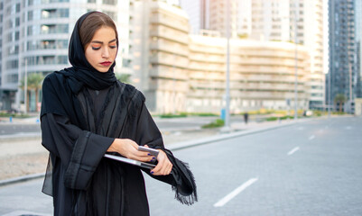 Wall Mural - Beautiful young muslim woman with laptop and phone on the street.