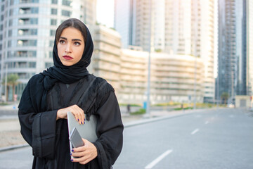 Wall Mural - Portrait of beautiful young Arabian woman holding laptop and phone on the street.