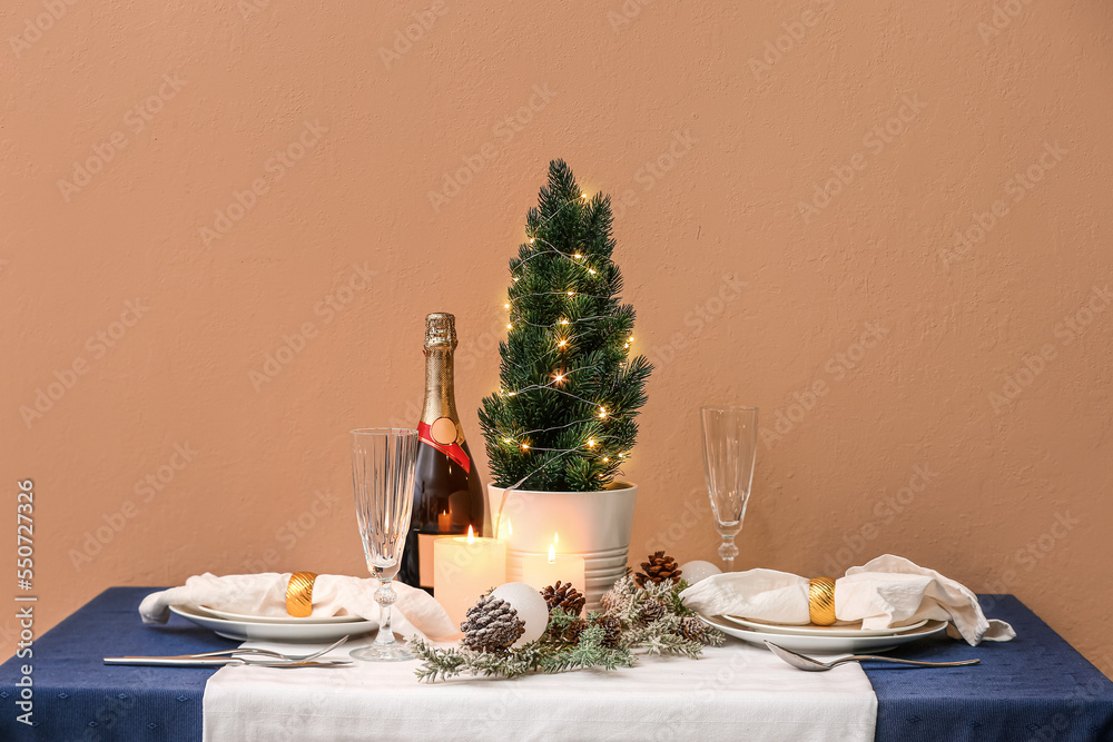 Table setting with small Christmas tree, fir cones and candles near beige wall