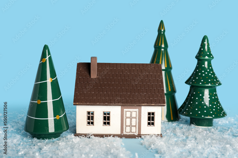 Composition with ceramic Christmas trees, house figure and snow on color background