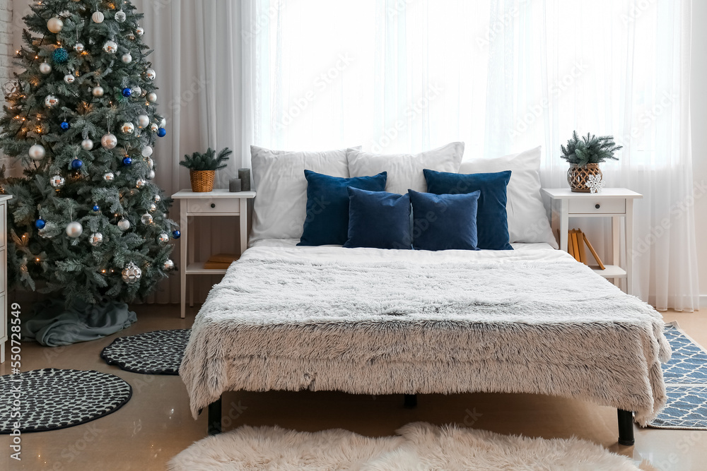 Interior of bedroom with glowing Christmas tree and tables