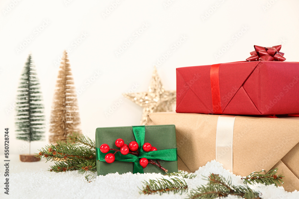 Christmas gift boxes with fir branches on snow against light background