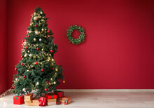 Glowing Christmas Tree With Presents And Wreath On Red Wall