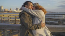 Couple With Pregnant Woman Hug And Kiss On Pier During Sunset