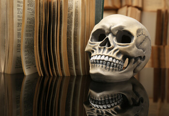 Human skull and old book on mirror table