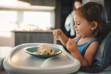 Happy baby girl looking at the tasty dessert on her plate. The child enjoy self eating meal sweet fruit and laughing happiness. Baby healthcare and nutrition