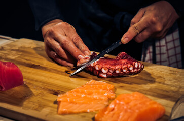 Wall Mural - Close up of Chef cook hands chopping octopus for traditional Asian cuisine with Japanese knife. Professional Sushi chef cutting seafood japanese chefs are making octopus sashimi. Dark Tone