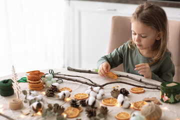 Winter holiday season. child little toddler girl making handmade Christmas garland home decorations from natural ECO materials