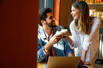 Wall Mural - Couple sitting at cafe smiling, using laptop, spending time with pleasure, drinking coffee.