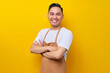 © Bangun Stock Photo - Optimistic young Asian man 20s barista employee wearing brown apron working in coffee shop, standing with crossed arms, looking on camera with toothy smile on yellow background. Small business startup