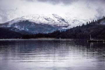 Poster - Scenic view of a tranquil lake surrounded by an evergreen forest and snow covered mountains