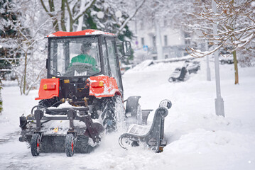 Wall Mural - Snow removal red tractor clean walkway in park with plough and sweeping brush. Tractor removing snow, cleaning sidewalk from snow during blizzard. Tractor clear snow, machinery cleaning equipment