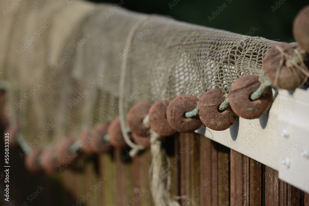 Fishing Net Railing Fishing net drying on a long wooden railing. We see the brown cork ...