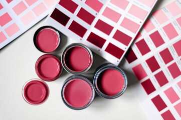 Tiny sample paint cans during house renovation, process of choosing paint for the walls, different red colors, color charts on background. Viva Magenta, color of the year 2023