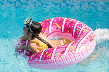 Smiling cute little caucasian girl in outdoor pool in sunny day. The girl is holding on to the side of the pool. Summer, vacation and health care concept