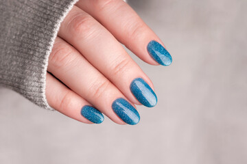 Wall Mural - Female hand in gray knitted sweater with beautiful manicure - blue glitter nails. Nail care concept