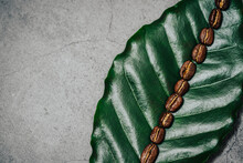 Roasted Coffee Beans Laying On A Green Coffee Leaf In A Row On Stone Background