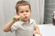© Leka - a boy of 3 years old holds a toothbrush and brushes his teeth in the bathroom, daily routine, dental care