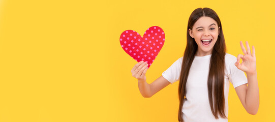 Canvas Print - winking kid hold love heart show ok gesture on yellow background, february 14. Kid girl portrait with heart love symbol, horizontal poster. Banner header with copy space.