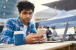 © Maria Vitkovska - Curly haired middle eastern man holding mobile phone, reading text message in cafe. Pensive successful freelancer using smartphone, laptop working online sitting at workplace. Technology concept