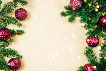 fir branches and purple christmas baubles with golden bokeh lights on beige background. top view, fl