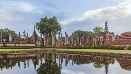 Wall Mural - Buddha statue and pagoda Wat Mahathat temple with reflection, Sukhothai Historical Park, Thailand - Time Lapse