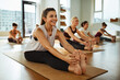 © Flamingo Images - Smiling woman touching her toes during yoga class