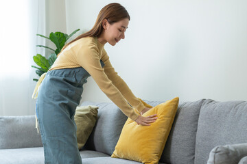 Wall Mural - Household clean up, housekeeper asian young woman, girl cleaning, hand keeping put pillow on sofa, couch in living room at home. Messy maid or housewife organizing dirty and untidy. Chore concept.