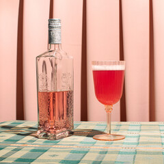 Pink gin bottle and a glass of red fizzy cocktail, retro style table cloth and pale pink drapery background. Vintage fashion style inspired house party idea. 