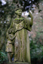 Historical Woman Figure With Child In An Old Cemetery Holding A Small Cross Like A Selfie Phone