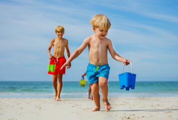 Wall Mural - Little boy run holding bucket on sand beach with friend