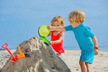 Boy and sister girl play with sand pour water from bucket