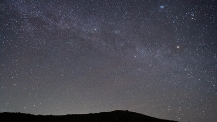 Wall Mural - The Milky Way Galaxy and Stars on Beautiful Dark Starry Night Sky 4K Time Lapse. Silhouette of Mountain Hill and Trees Background.