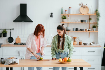 two girlfriends cut fruit in the kitchen