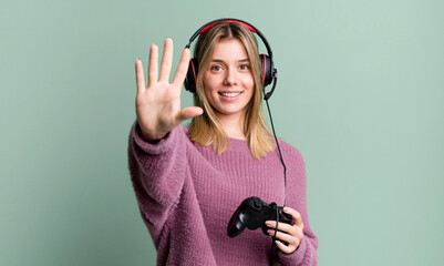 young pretty woman smiling and looking friendly, showing number five. gamer with headset and controller