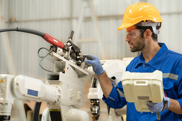 Wall Mural - Male industrial engineer using remote control board to check robotic welder operation in modern automation factory. Technician worker monitoring robot controller system for automated steel welding.