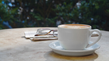 Wall Mural - Cup of delicious coffee, glasses and newspaper on beige marble table outdoors, space for text