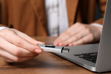 Woman Holding Usb Flash Drive Near Laptop At Wooden Table, Closeup