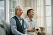 asian seniior father and adult son watching football match on tv together