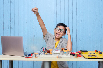 Smart looking Asian boy working with circuits, wires, computer, motor on his project. Science, Technology, Engineering and Mathematics (STEM) education concept.