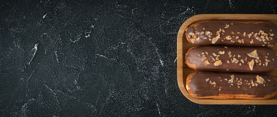 Wall Mural - Eclair with custard and chocolate icing on black concrete background. Traditional French pastry. Eclair with cream filling covered with melted milk chocolate. Flat lay