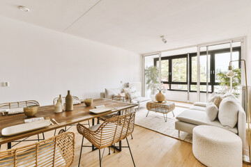 Contemporary minimalist style interior design of light studio apartment with wooden table and chairs in dining zone between open kitchen and living room with white walls and parquet floor