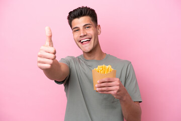 Young caucasian man holding fried chips isolated on pink background with thumbs up because something good has happened