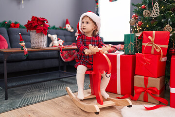 Sticker - Adorable hispanic girl playing with reindeer rocking by christmas tree at home